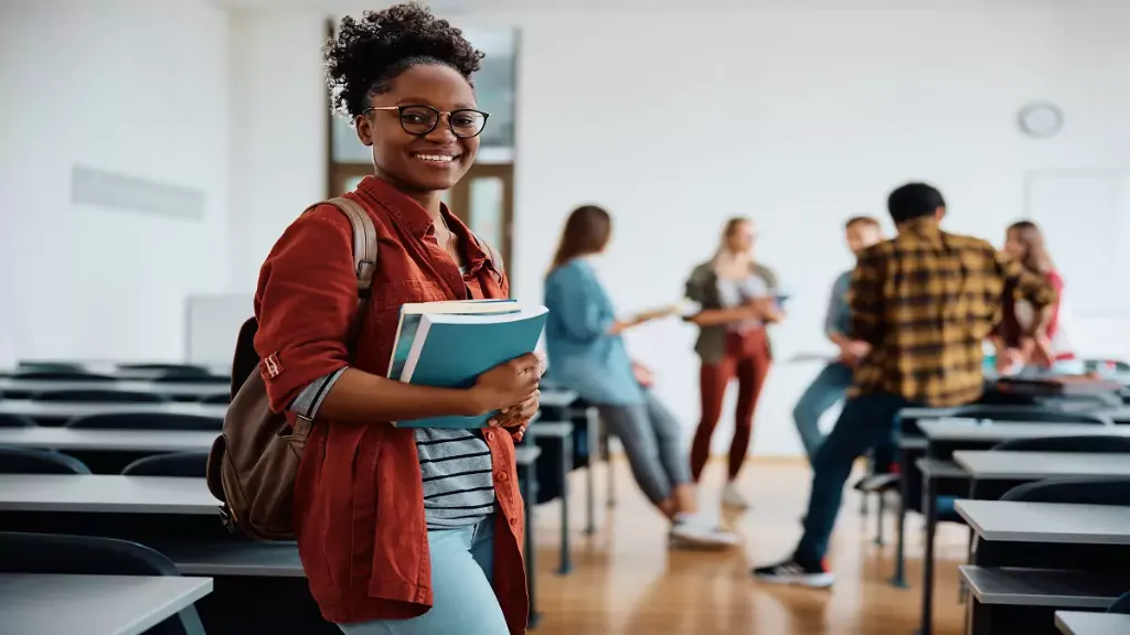 Aluna sorrindo com livros em sala de aula